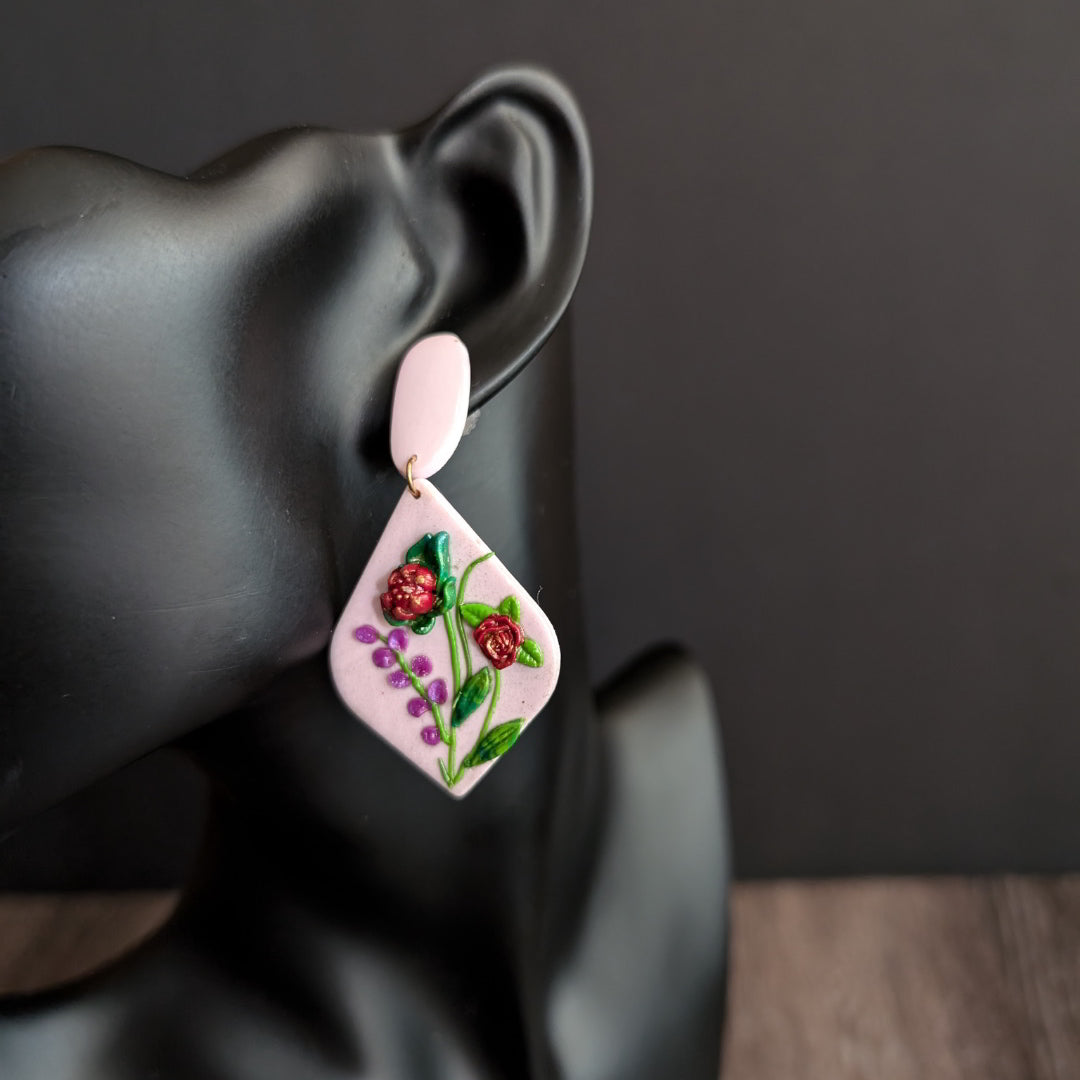 Handcrafted light pink floral earrings with red blooms, green leaves, and small pink flower accents.