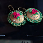 Handcrafted floral medallion earrings with green bezel and golden center adorned with roses and leaves.