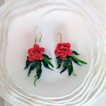 Handcrafted polymer clay Blooming Hibiscus Dangle Earrings with red flowers, green leaves, trailing vines, and ceramic plate accents for added elegance